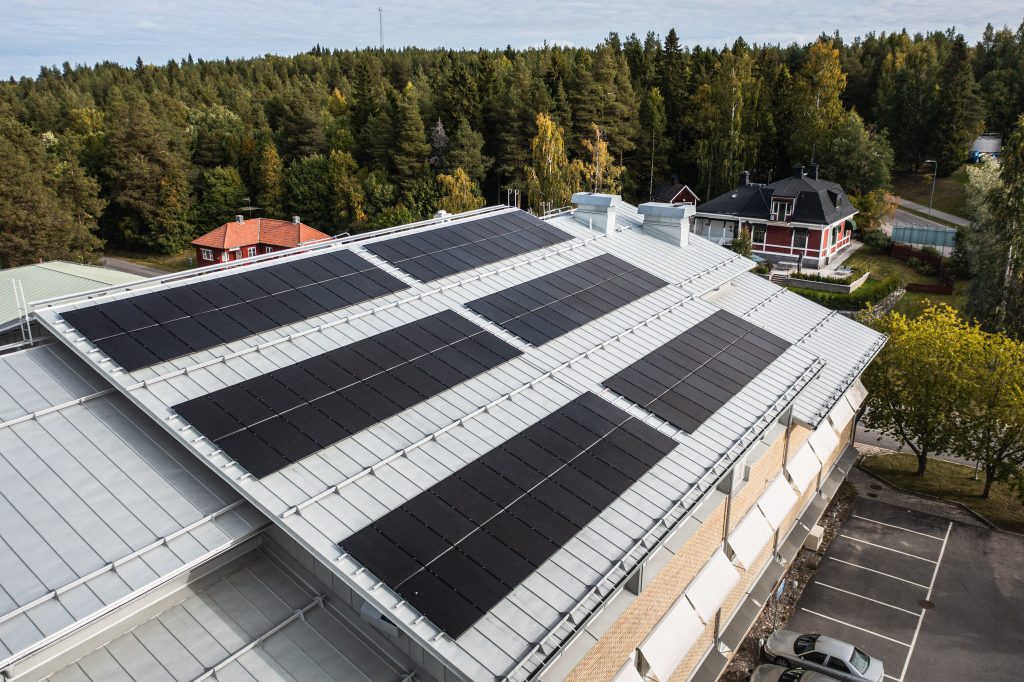 Solcellspaneler är monterade på ett tak som syns i förgrunden. De mörka panelerna täcker en stor del av taket.