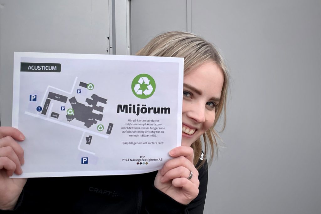 En kvinna håller upp en karta som visar vägen till miljörummet. Hon kikar fram bakom pappret. I bakgrunden syns en grå dörr.