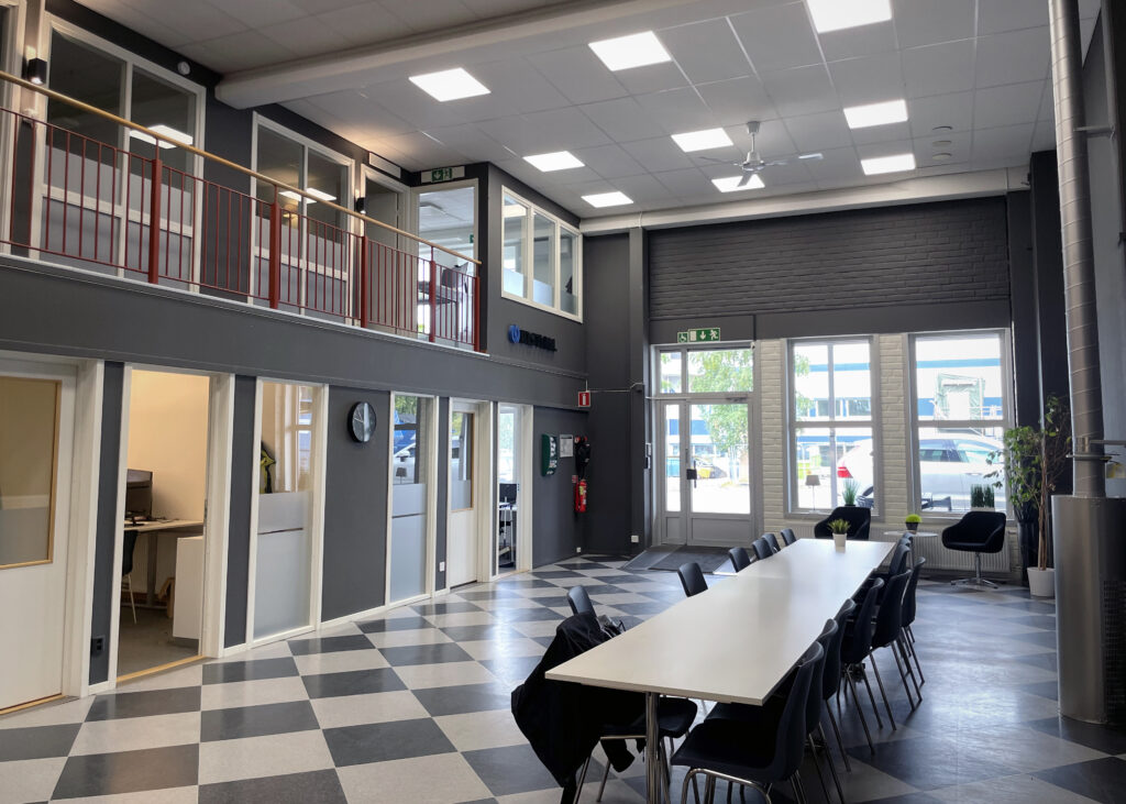 Ljus, luftig entré med högt i tak. Genom stora glaspartier flödar dagsljuset in och rummet öppnar sig mot utsidan. Mitt i lokalen står ett långt bord som samlingspunkt.