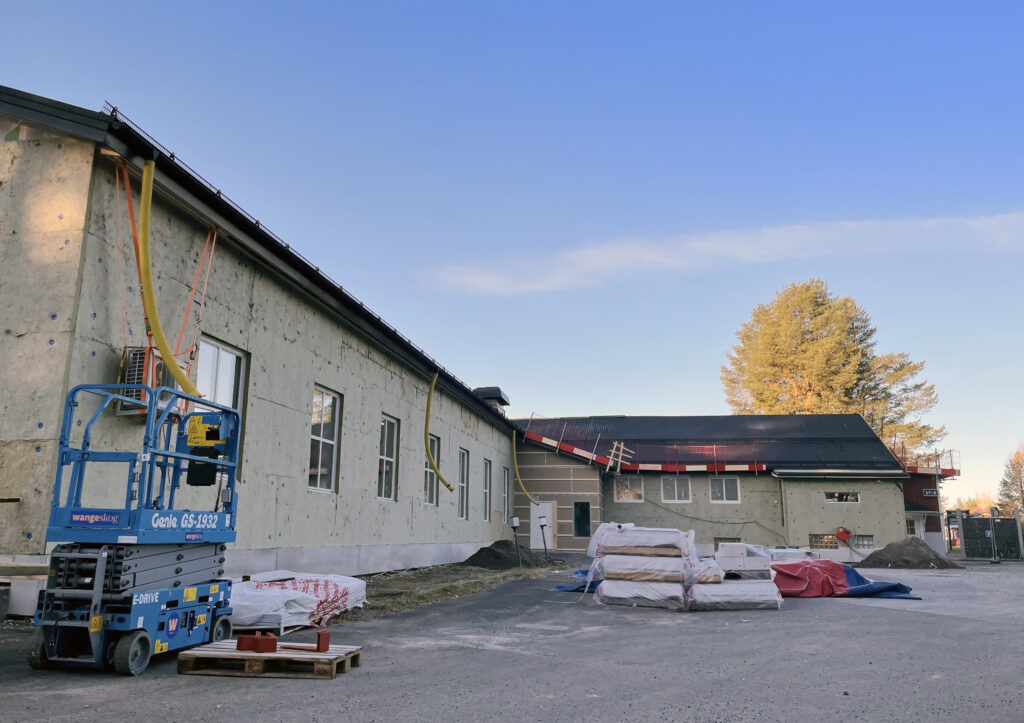 Klar blå himmel ovanför en byggnad med ställningar längs väggarna. Renovering och förbättrad isolering pågår.