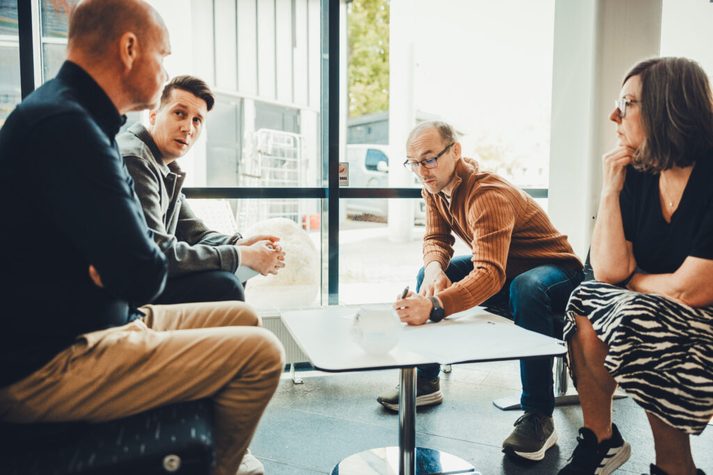Tre personer sitter i en workshop och möts i ett engagerat samtal där de ser på varandra med fokus och en lugn, koncentrerad känsla i bilden.