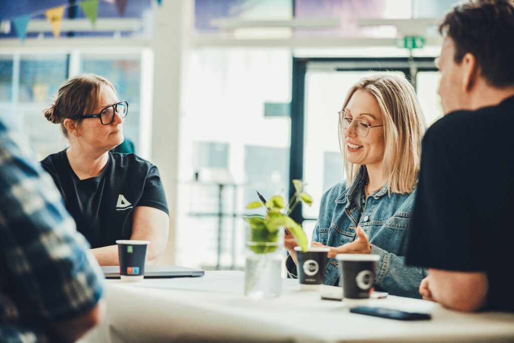 Två kvinnor sitter i en workshop och deltar i ett engagerat samtal medan den tredje personen lyssnar intill och stämningen är fokuserad och lugn.