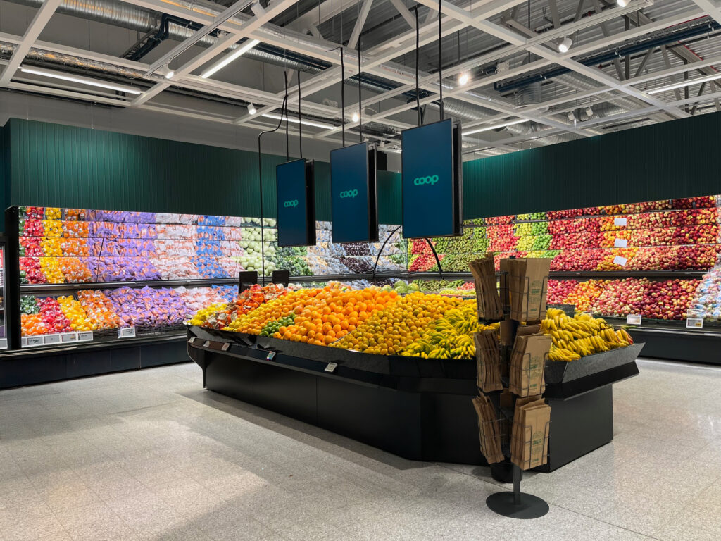 Stilrent butiksfoto med fruktavdelningen i fokus. Varor och inredning framhävs tydligt i en ljus miljö där hyllor och färsk frukt formar helheten.