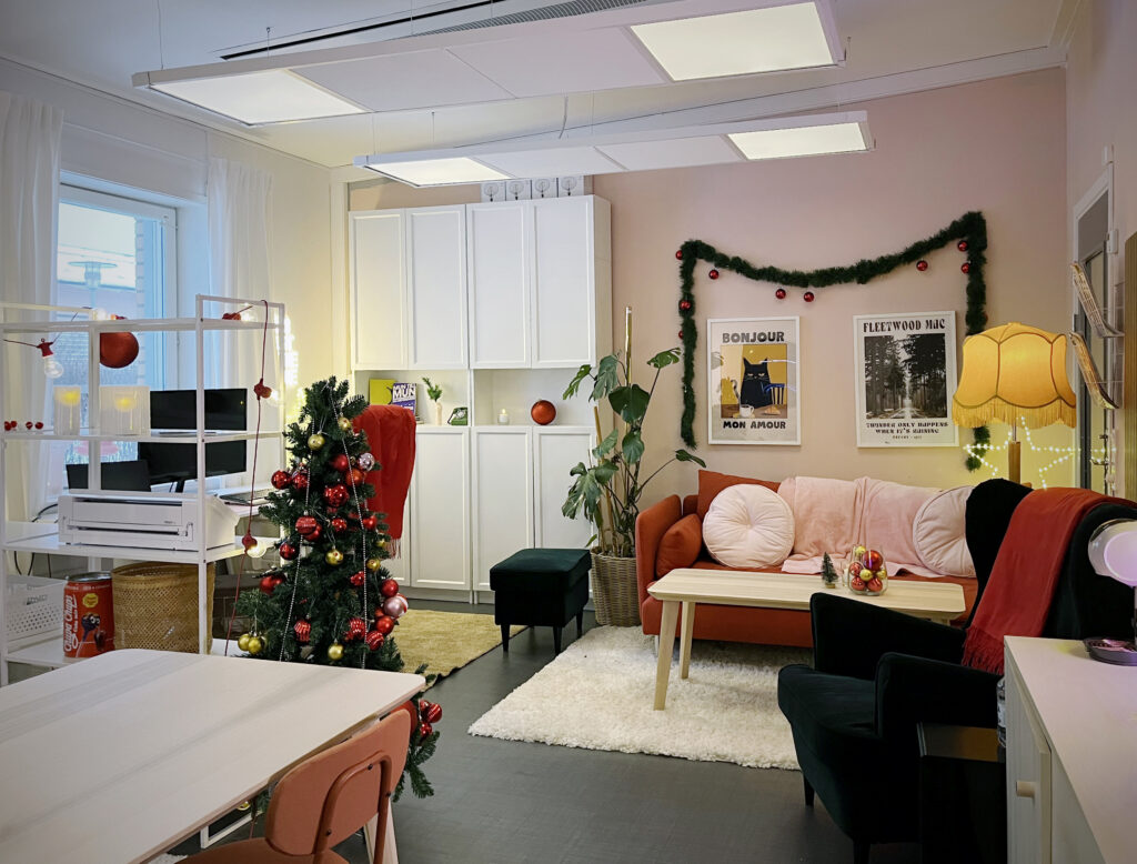 Överblick av ett inrett rum med soffa, fåtöljer och julgran. Röda och gröna detaljer, ljusslingor och tavlor skapar en varm, inbjudande stämning.