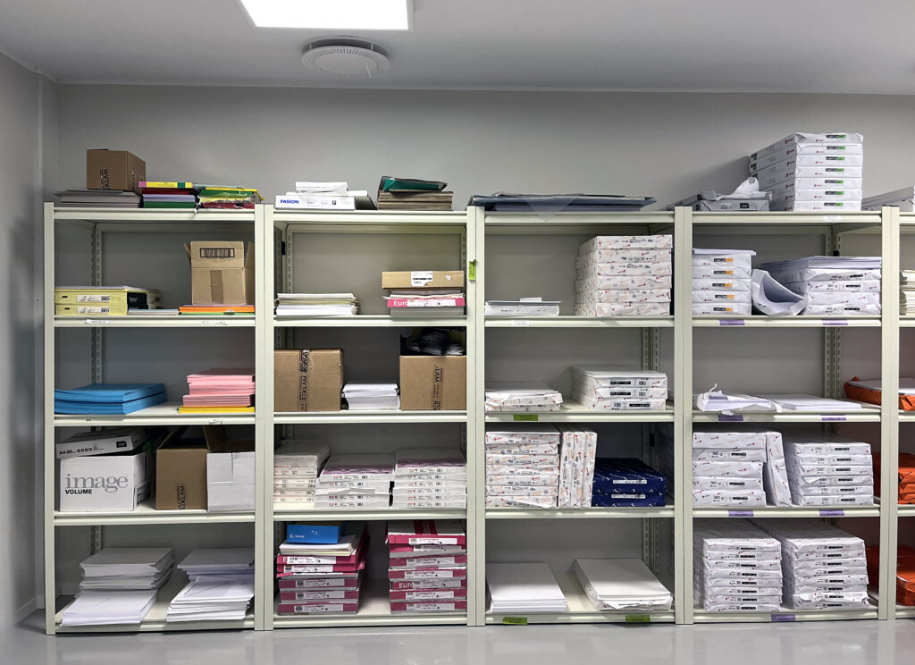 Ett välordnat hyllsystem fyllt med olika typer av arbetsmaterial står mot ljusgrå golv. Tydliga rader och rena ytor ger en lugn, strukturerad känsla.