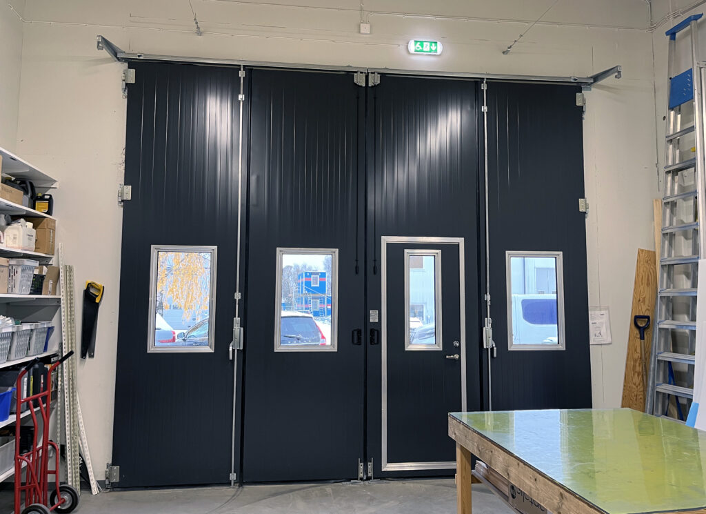 Svart port lyfts fram mot ljusgrå väggar i ett garage med högt i tak. Rummet känns luftigt med öppna ytor och ett stilla, mjukt ljus som faller över ytan.