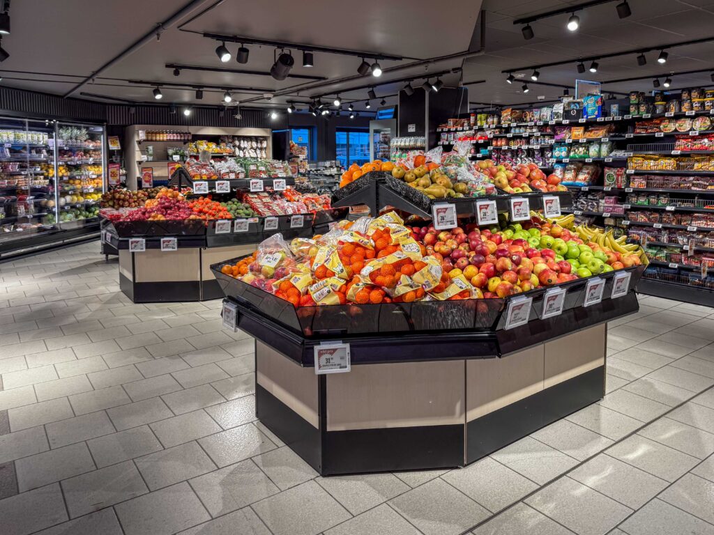 Interiör av fruktavdelning i matbutik med tydlig takbelysning som lyser upp prydliga upplägg. Stilrent och snyggt i en ljus miljö.