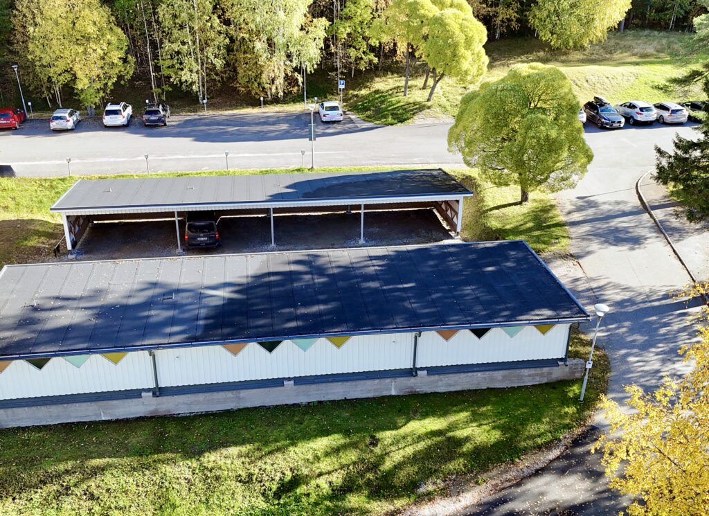 Drönarbild över Furunäset med carport, parkerade bilar och grönskande träd i höstsol.