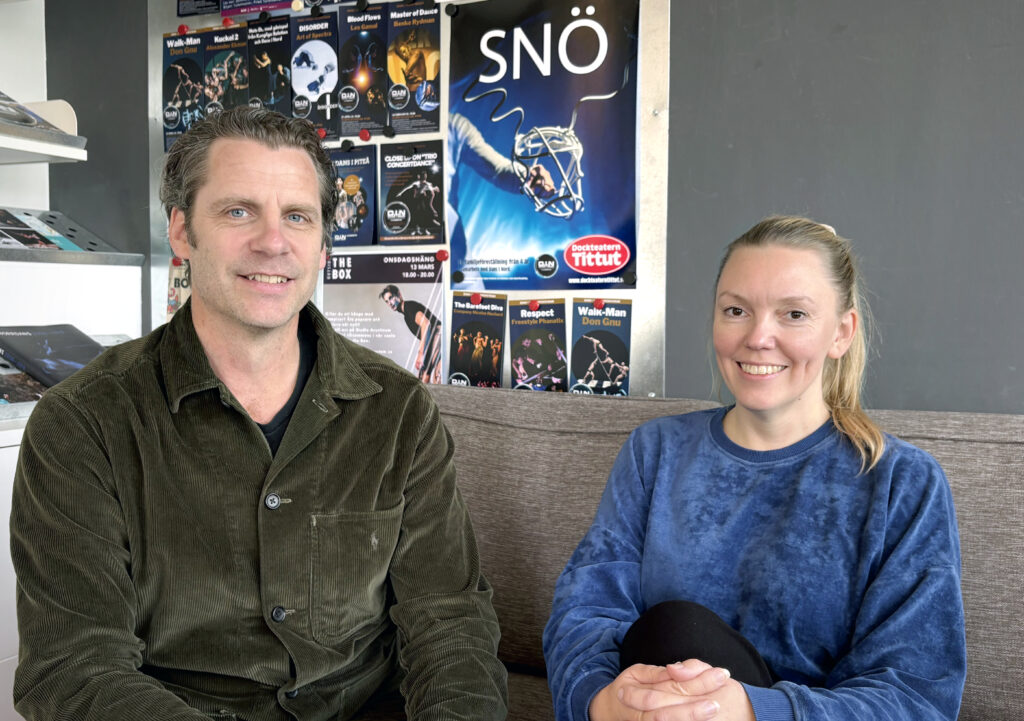 Olof Westring och Marielle Marklund från Dans i Nord sitter i en soffa framför en vägg med färgstarka dansaffischer.
